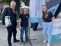 Kreissportbund Wesel Zwei Mitarbeiterinnen des Kreissportbundes stehen mit einem Mann, der einen Musikkoffer trägt, vor einer Beachflag des Kreissportbund Wesel.