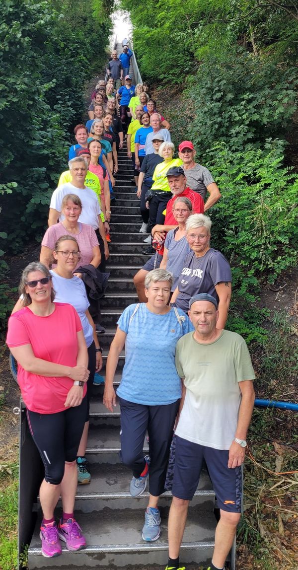 Gruppe von Menschen steht auf einer langen Außentreppe, umgeben von dichtem Grün an beiden Seiten.