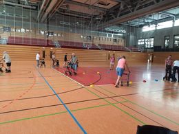 Sicher unterwegs mit dem Rollstuhl oder Rollator Mehrere Menschen mit einem Rollator fahren durch eine Turnhalle. Einige von ihnen fahren um bunte Hütchen.