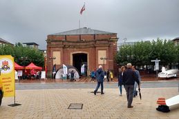 Einige Menschen laufen bei regnerischem Wetter vor dem Stand des Kreissportbundes. Im Hintergrund ist das Berliner Tor in Wesel zu sehen.