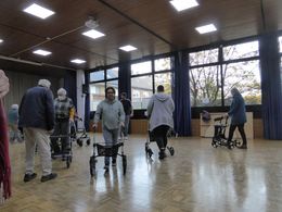 Aktionstag sicher unterwegs mit dem Rollstuhl und Rollator Eine Gruppe Menschen fährt mit Rollatoren durch eine Turnhalle.