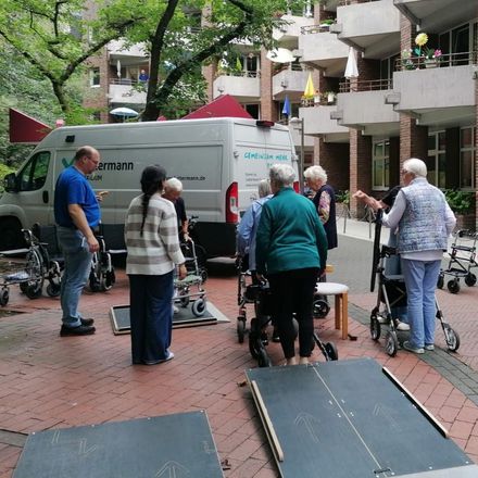 Eine Gruppe Senioren steht in einem Rollatorparcours vor einem Kleinbus von Luttermann