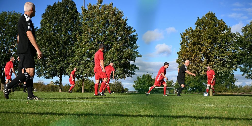 Fußballspieler in roten und schwarzen Trikots auf einem Spielfeld mit Bäumen im Hintergrund.