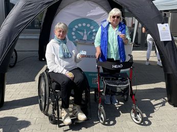 Erfolgreich mit dem Rollstuhl, bzw. Rollator den Parcours bewältigt. Herzlichen Glückwunsch! Eine Rollstuhlfahrerin und eine Rollatornutzerin vor dem Kreissportbundpavillon mit dem Rollator- und Rollstuhlführerschein in der Hand.