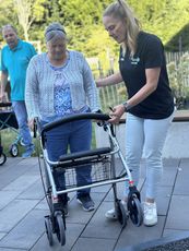Auf die richtige Nutzung kommt es an. Eine ältere Frau mit einem Rollator wird von einer Mitarbeiterin des KSB unterstützt. Die ältere Frau trägt einen grauen Pullover und ein gemustertes Oberteil. Die jüngere Frau trägt ein schwarzes T-Shirt und eine helle Hose.