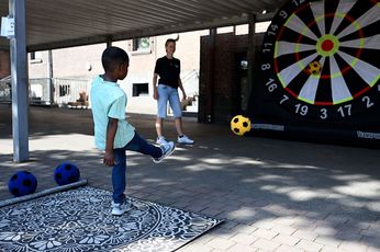 Motiviert beim Fußballdarts. Ein kleiner Junge im türkisen T-Shirt und blauer Jeans schießt einen gelben Ball auf eine überdimensional große Dartscheibe. Eine Mitarbeiterin des Kreissportbundes schaut ihm dabei zu.