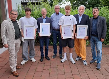 Bürgermeister Dietmar Heyde, Ehrenamtler Luca Simon und Wilhelm Wens, stellvertretender KSB-Vorsitzender Ulrich Glanz, Ehrenamtler Aaron Jendro und Clemens Brune sowie SSV-Vorsitzender Frank Tatzel stehen nebeneinander auf einem gepflasterten Hof, die vier Geehrten halten gerahmte Urkunden, alle tragen legere bis formelle Kleidung.