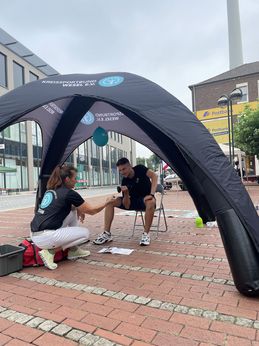 Ein Mitarbeiter des Kreissportbundes trainiert mit einer Hantel seinen Bizeps, während eine Mitarbeiterin des Kreissportbundes ihm dabei Tipps gibt.