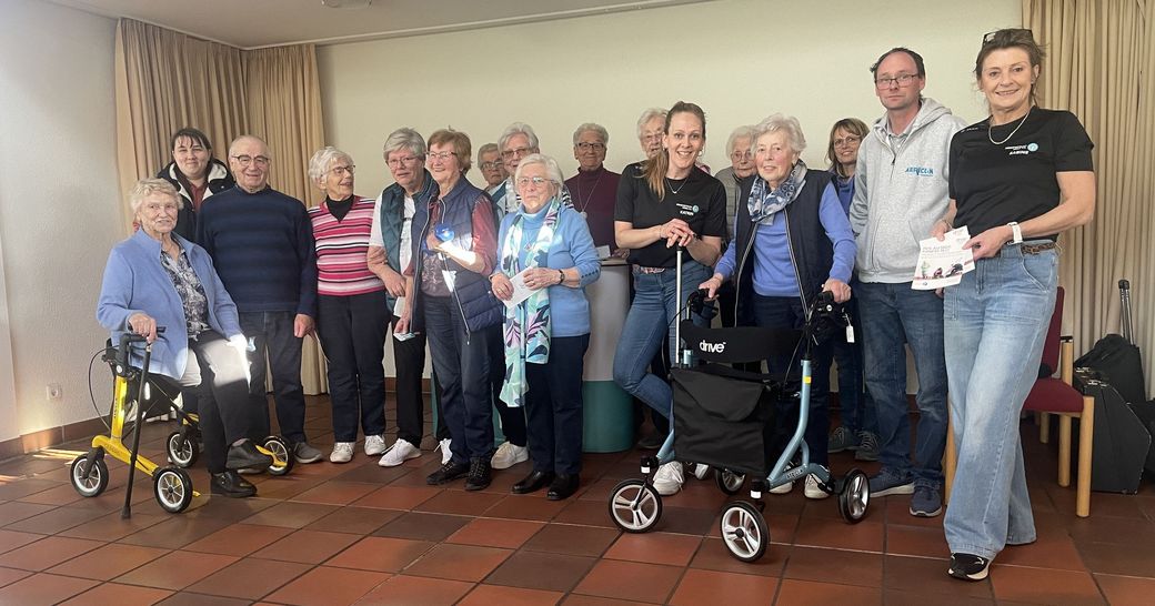 Seniorennachmittag in Alpen-Veen am 2. April 2025 Eine Gruppe Seniorinnen und Senioren, teilweise mit Rollatoren, die Rollatorführerscheine und Präsente in den Händen halten. Zwei Mitarbeiterinnen des Kreissportbundes und der Firma Aericon stehen zwischen den Seniore*innen.