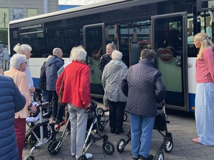 Eine Gruppe Senioren steht neben einem Linienbus mit geöffneten Türen und hört einer Dame zu, die das Ein- und Aussteigen erklärt.