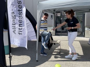 Konzentriert beim Alltags-Fitness-Test Ein älterer Herr im gestreiften T-Shirt, der sein Knie anhebt. Davor eine Mitarbeiterin des Kreissportbundes, die mit einem Zähler die Wiederholungen zählt.