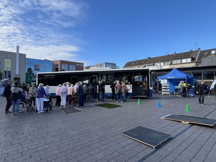 Ein Linienbus steht auf einem Marktplatz, davor stehen Senioren mit ihren Rollatoren. Im Vordergrund ist ein Rollatorparcours zu sehen.