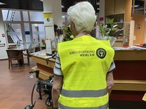 Gut sichtbar in der Dunkelheit Eine ältere Dame, die mit dem Rücken zur Kamera steht. Sie trägt eine gelbe Warnweste mit dem Logo Kreissportbund Wesel e.V.. Vor ihr steht ein Rollator.