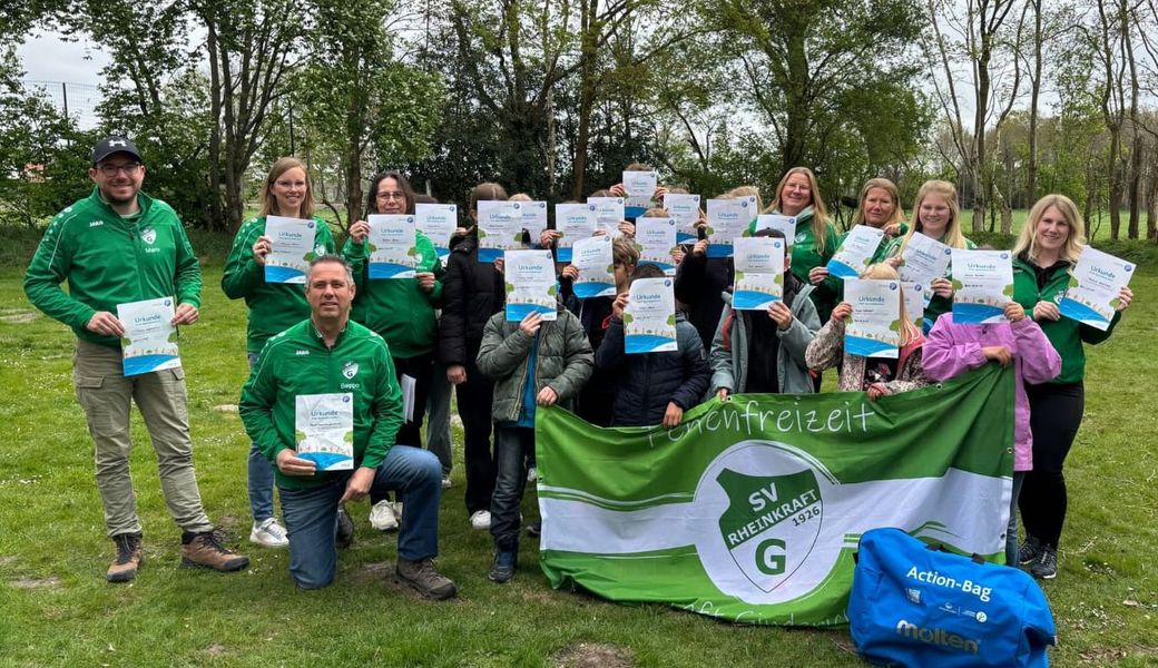 Gruppe von Kindern und Jugendlichen im Freien, die Urkunden hochhalten, davor eine grün-weiße Fahne mit dem Schriftzug 'SV Ginderich'.