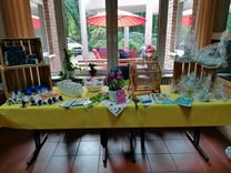 Aktionstag "Sicher unterwegs" Ein Tisch mit einer gelben Tischdecke, auf dem eine Lostrommel und diverse Präsente, wie Fahrradklingeln, Warnwesten, Flyer, Blumen und Handtücher stehen.