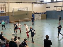 Mehrere Männer spielen Walking Football in einer Sporthalle.
