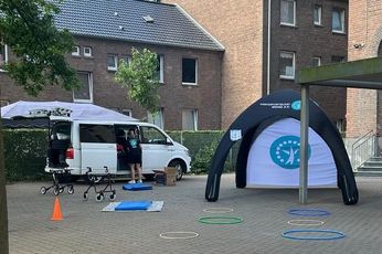 Der Rollstuhl- und Rollatorparcours wartet auf die ersten Teilnehmer. Der Stand des Kreissportbund Wesel. Im Hintergrund eine Mitarbeiterin des Kreissportbundes vor einem weißen Van und ein Zelt des Kreissportbundes. Im Vordergrund liegen Holzreifen, Matten und Pylonen.