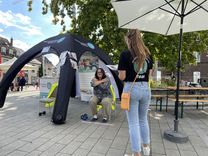 Alltags-Fitness-Test Ein Zelt des Kreissportbundes, eine Frau sitzt mit den Armen über Kreuz vor ihrem Körper und den Händen an den Schultern auf einem Stuhl sitzend, während eine Mitarbeiterin des Kreissportbundes vor ihr steht und erklärt.