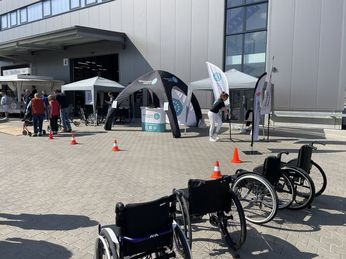 Rollstuhl- und Rollatortag in Wesel Aufbau der Aktionsfläche mit Pavillon, Zelt des Kreissportbundes und Rollatoren im Vordergrund. Im Hintergrund ein Rollatornutzer mit seiner Frau und dem Referenten, der einen Rollatorparcours durchläuft.
